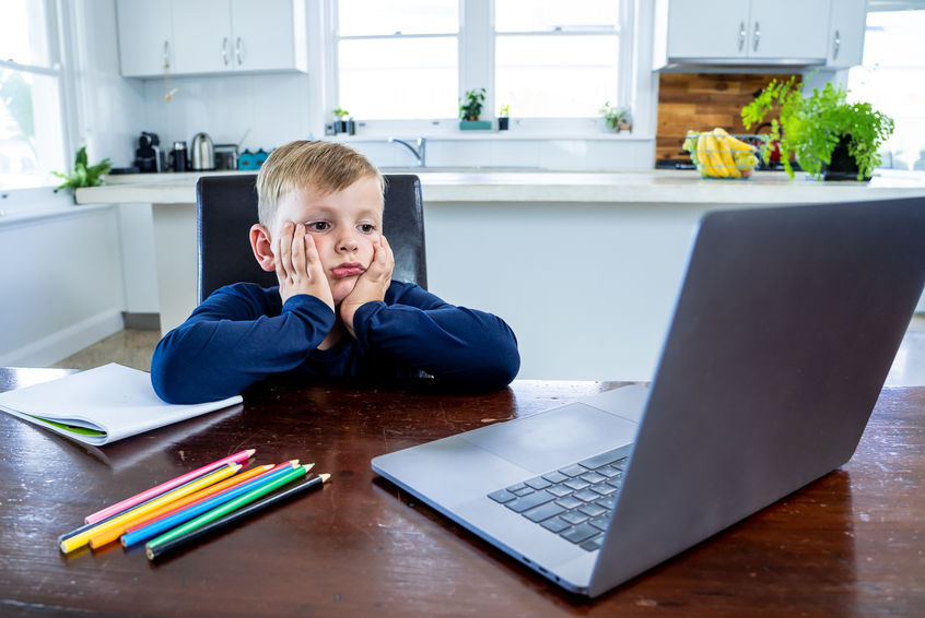Coronavirus school closures and lockdown. Bored kid with face mask studying online class at home