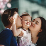 Happy young parents with a little daughter stand under blooming