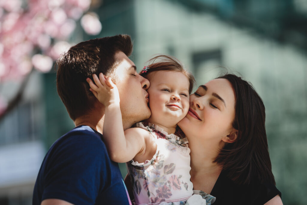 Happy young parents with a little daughter stand under blooming