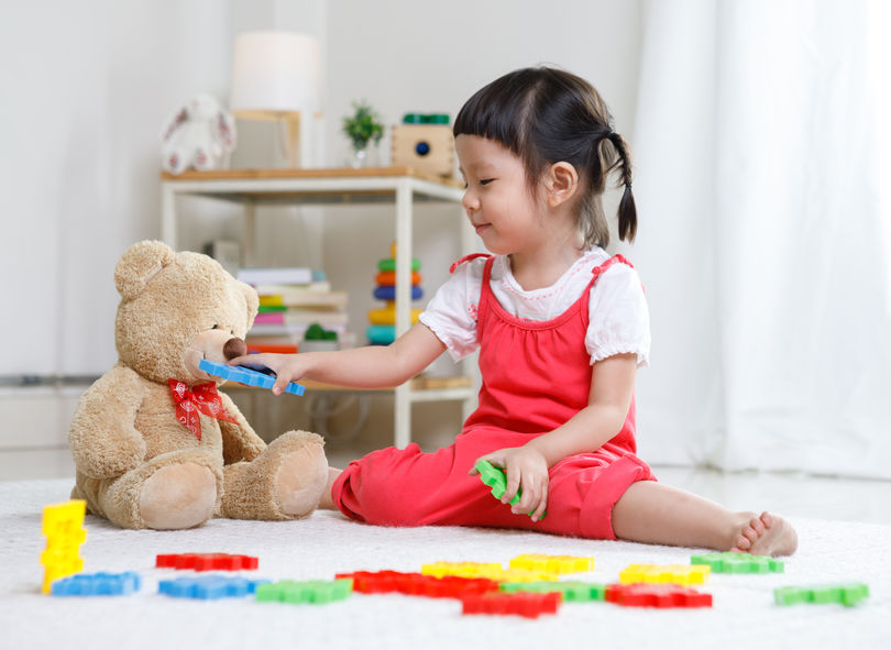 Preschooler girl learns at school. Cute child playing with teddy