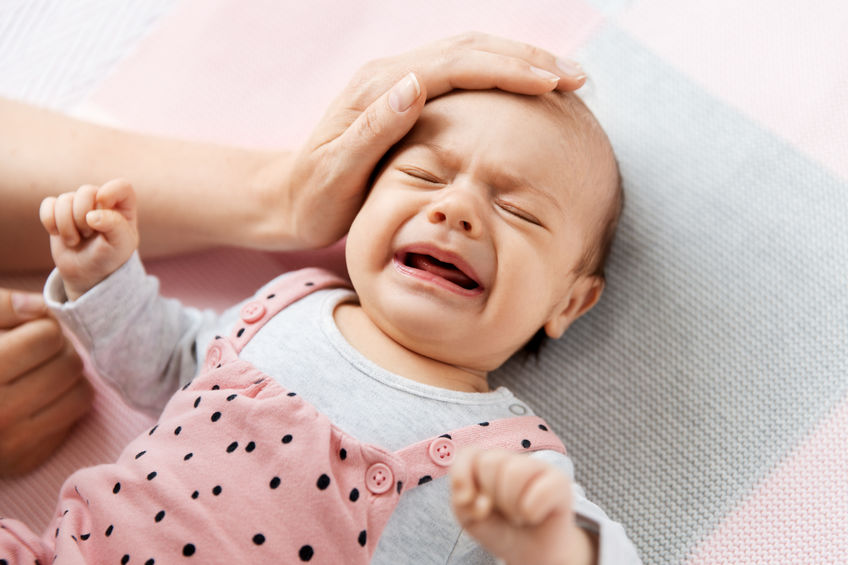 mother’s hand touching crying little baby daughter