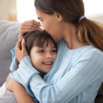 Loving mother hugging little daughter kissing kid sitting on sof