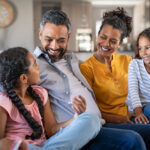 happy parents on couch with daughters, Get on the Same Page: Practical Steps to Resolve Parenting Style Conflicts